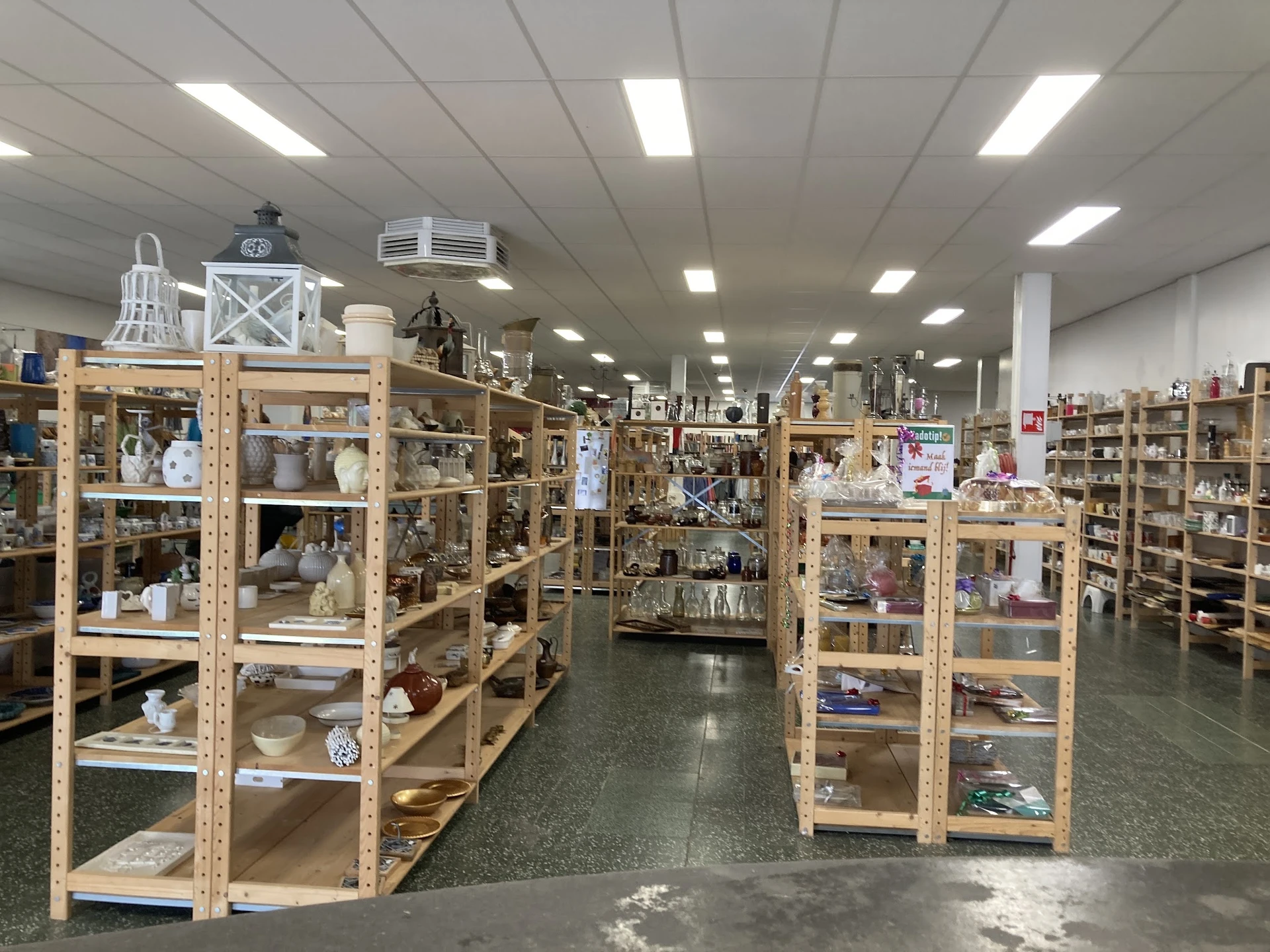 Winkelvloer met houten stellingen vol serviesgoed, decoratie en huishoudelijke artikelen in een kringloopwinkel