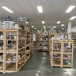 Winkelvloer met houten stellingen vol serviesgoed, decoratie en huishoudelijke artikelen in een kringloopwinkel