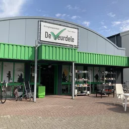 Gevel van kringloopwinkel De Veurdele met groene metalen wanden, etalageramen en ingang aan Hellingstraat