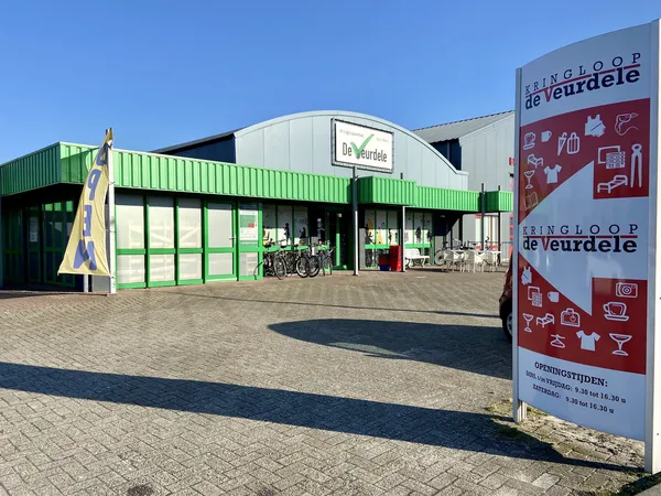 Gevel van kringloopwinkel De Veurdele met groene golfplaten gevel en winkelnaam op het dak