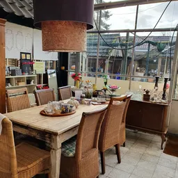 Eetkamer met houten tafel, rieten stoelen en grote ramen met uitzicht op straat