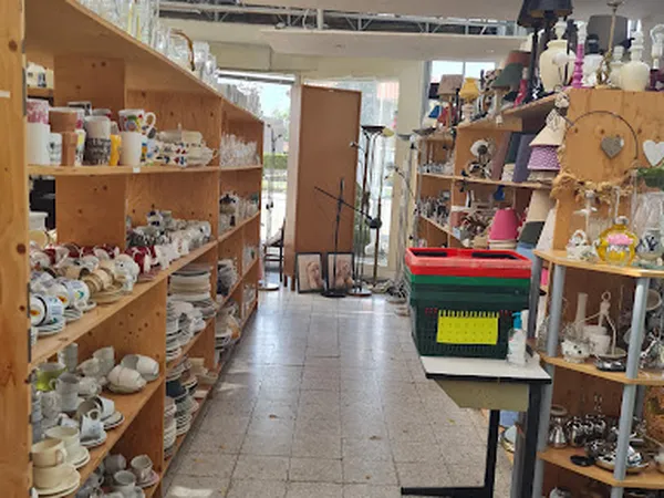 Binnenaanzicht van kringloopwinkel met houten stellingen vol serviesgoed en huishoudspullen