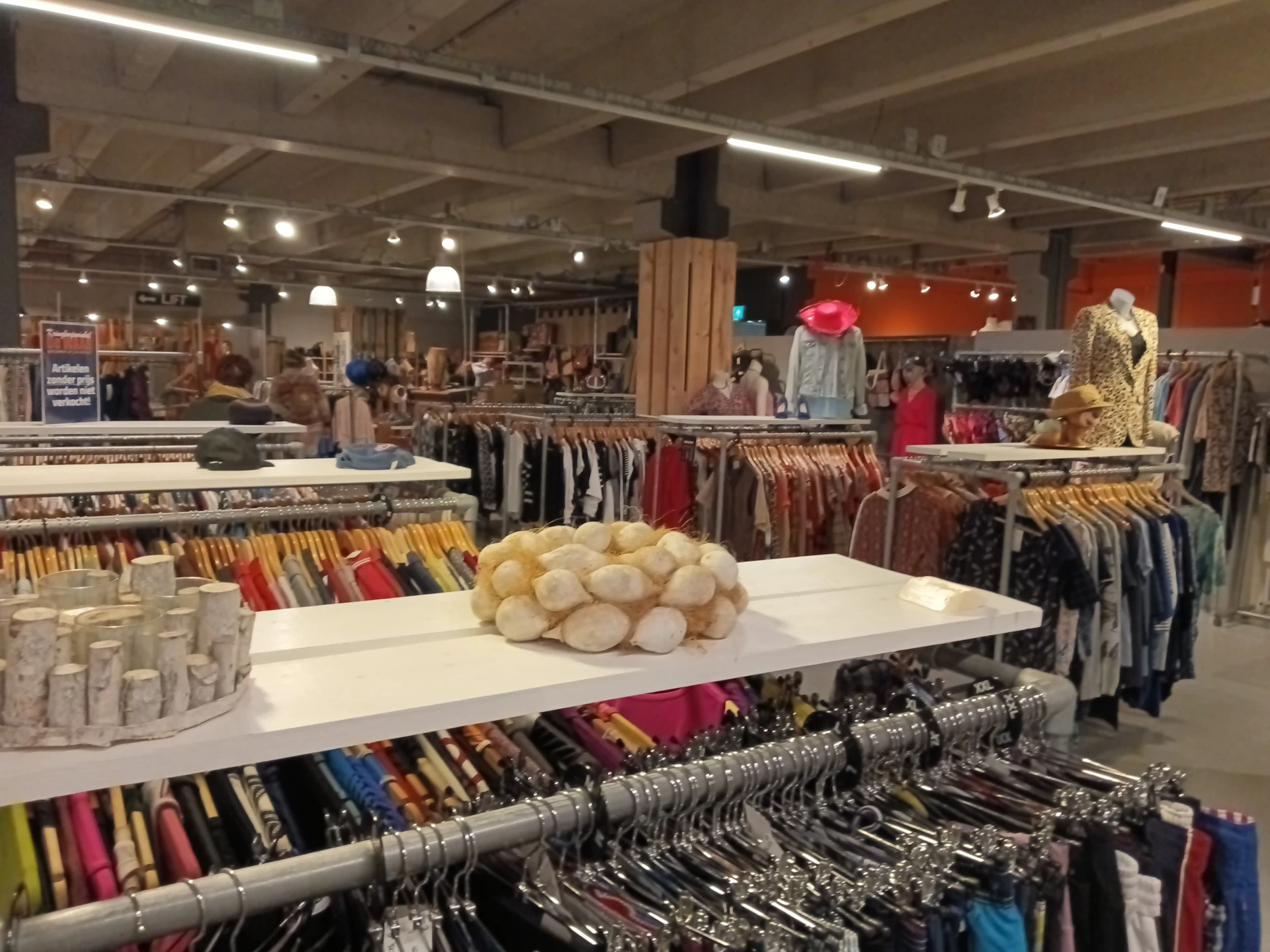 Winkelvloer met kledingrekken, stellingen met accessoires en decoratieve items in kringloopwinkel
