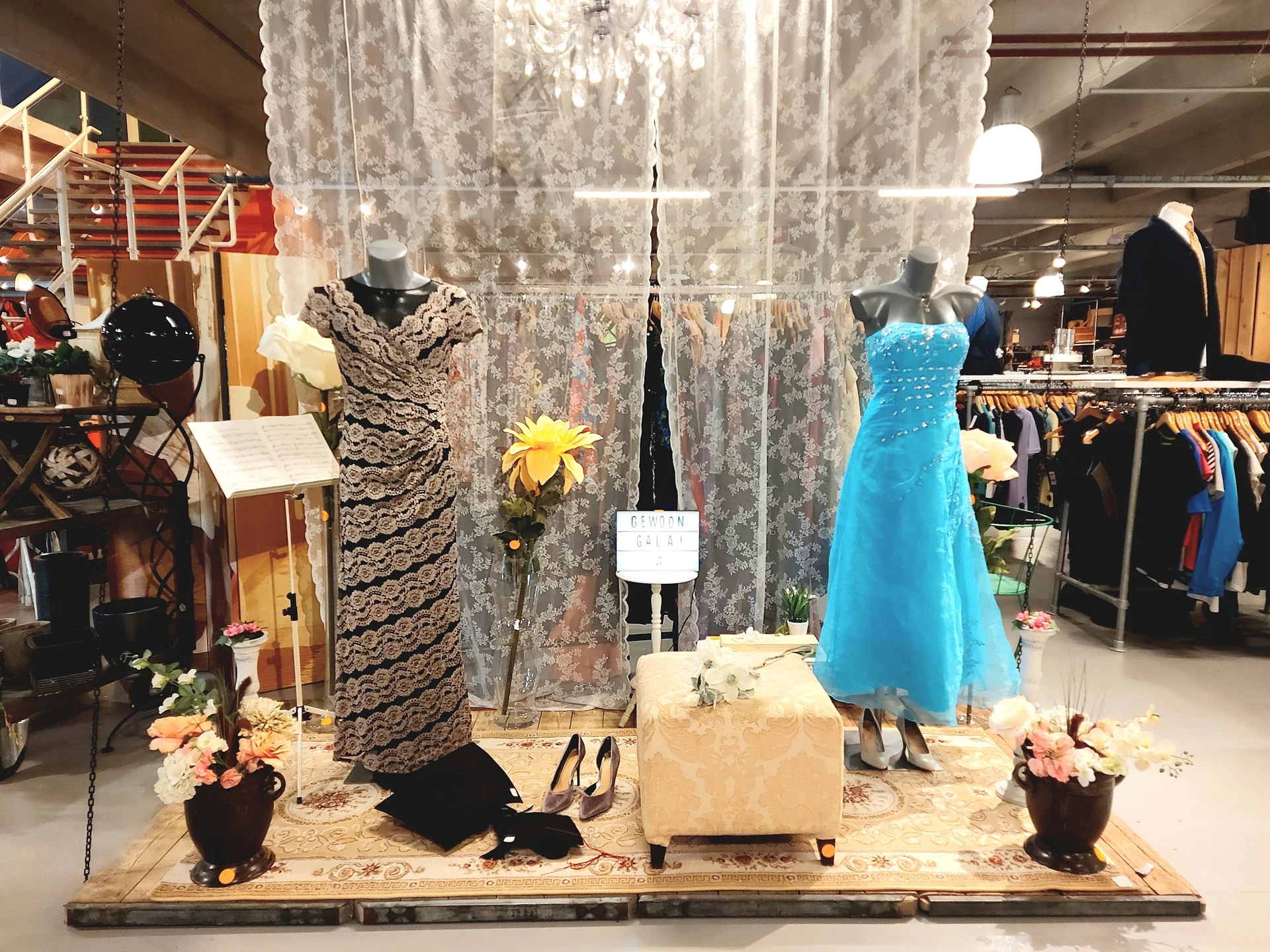 Etalage met dameskleding op mannequins, waaronder een zwart-witte jurk en blauwe avondjurk, versierd met bloemen