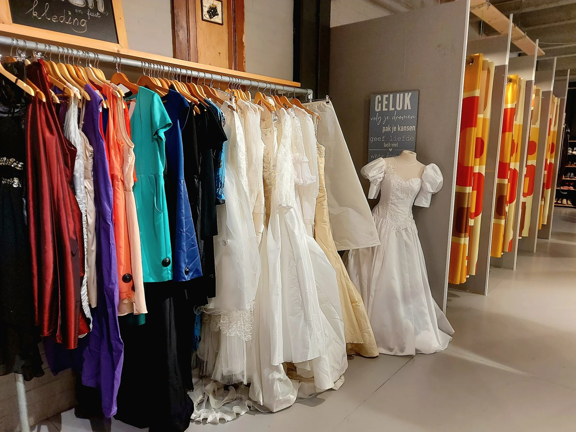 Rekken met tweedehands dameskleding in verschillende kleuren en witte trouwjurken op display