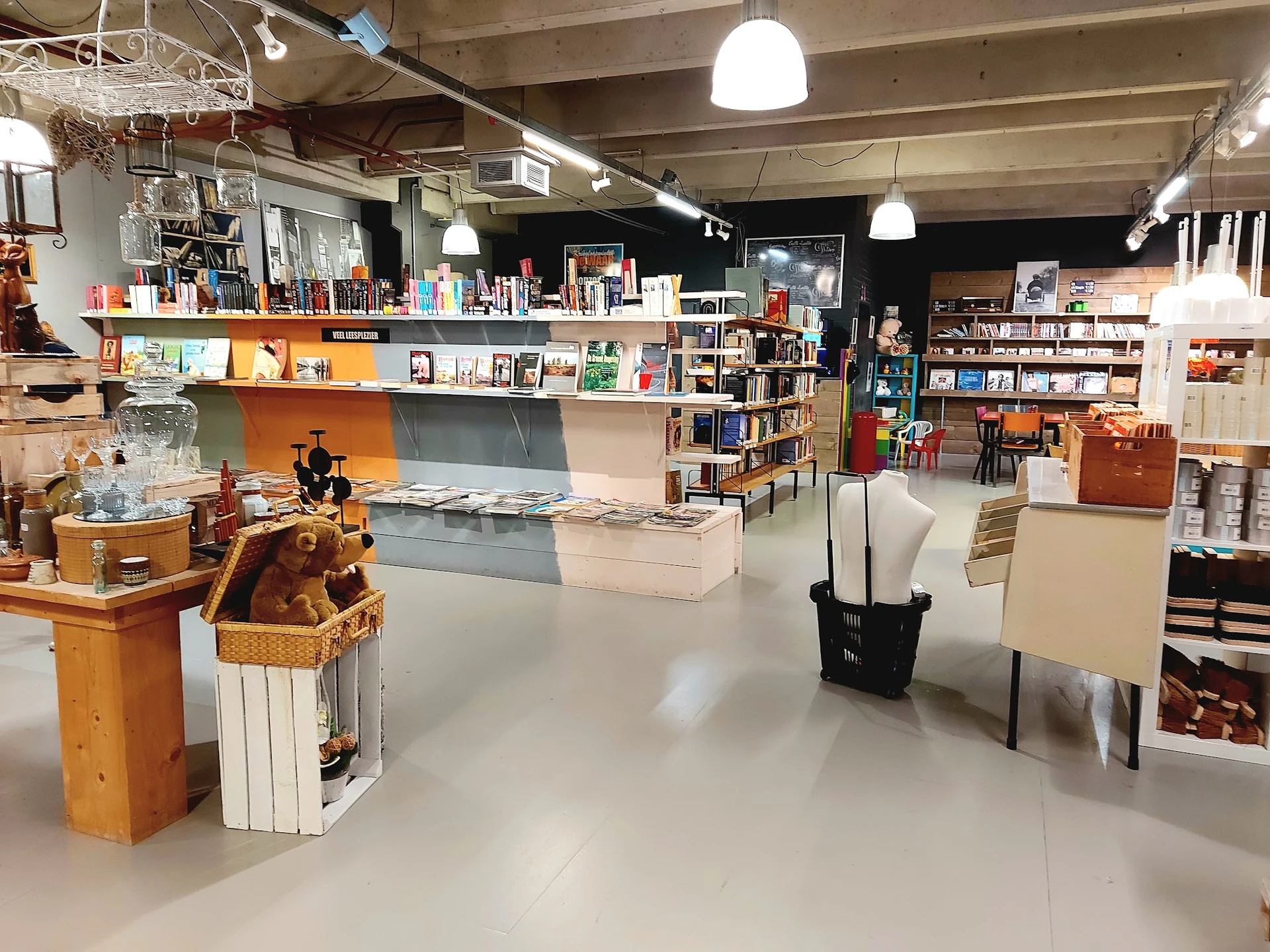 Ruime winkelvloer met boekenrekken, toonbanken en uiteenlopende spullen in een kringloopwinkel