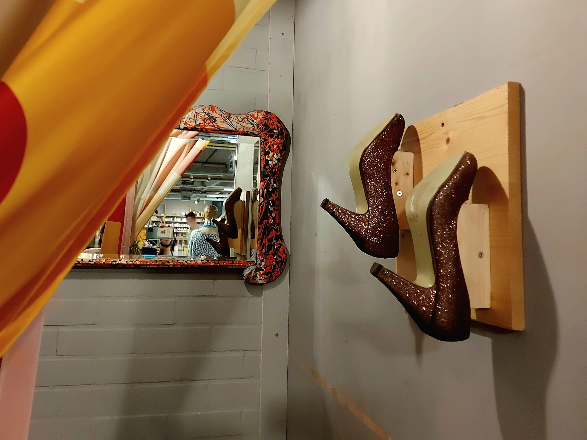 Spiegelkast en houten schoenenrekje met bruine glitterschoenen tegen witte muur