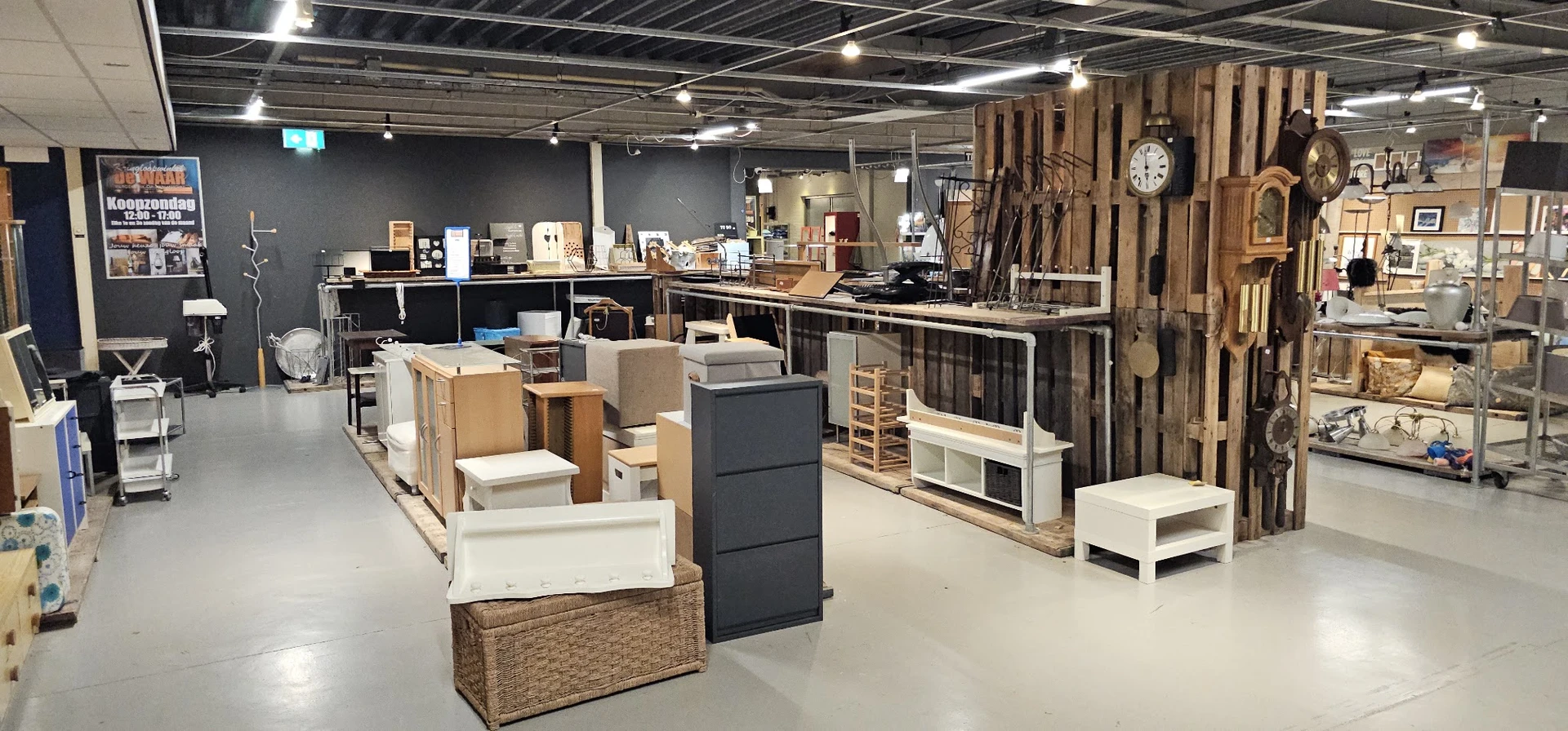 Winkelvloer met diverse meubels en huisraad uitgestald, stellingen met gereedschap en decoratie aan de wand