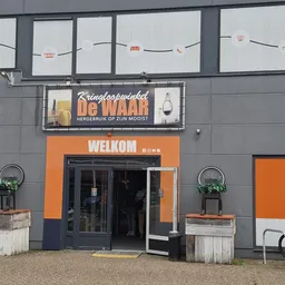 Gevel van kringloopwinkel De Waar met oranje accenten, winkelnaam op bord en ingang met glazen deuren