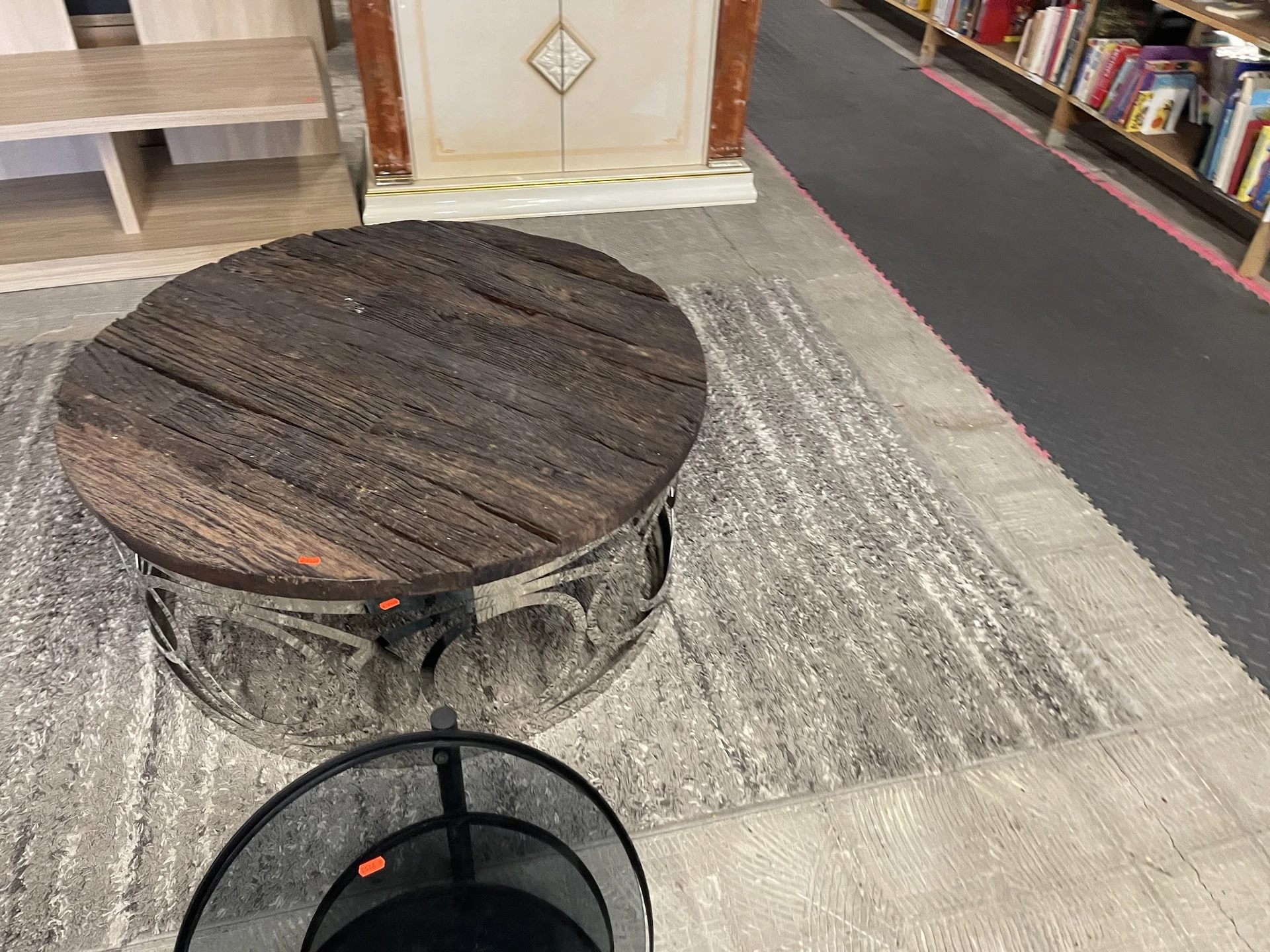 Ronde houten tafel en zwarte metalen voetstuk op display in kringloopwinkel