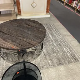 Ronde houten tafel en zwarte metalen voetstuk op display in kringloopwinkel