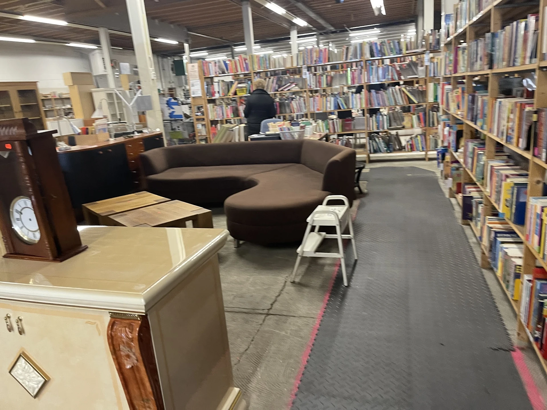 Winkelruimte met boekenrekken, bruine ronde zitbank en houten meubels op grijze vloer