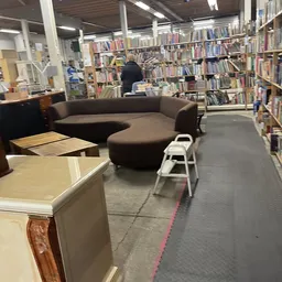 Winkelruimte met boekenrekken, bruine ronde zitbank en houten meubels op grijze vloer