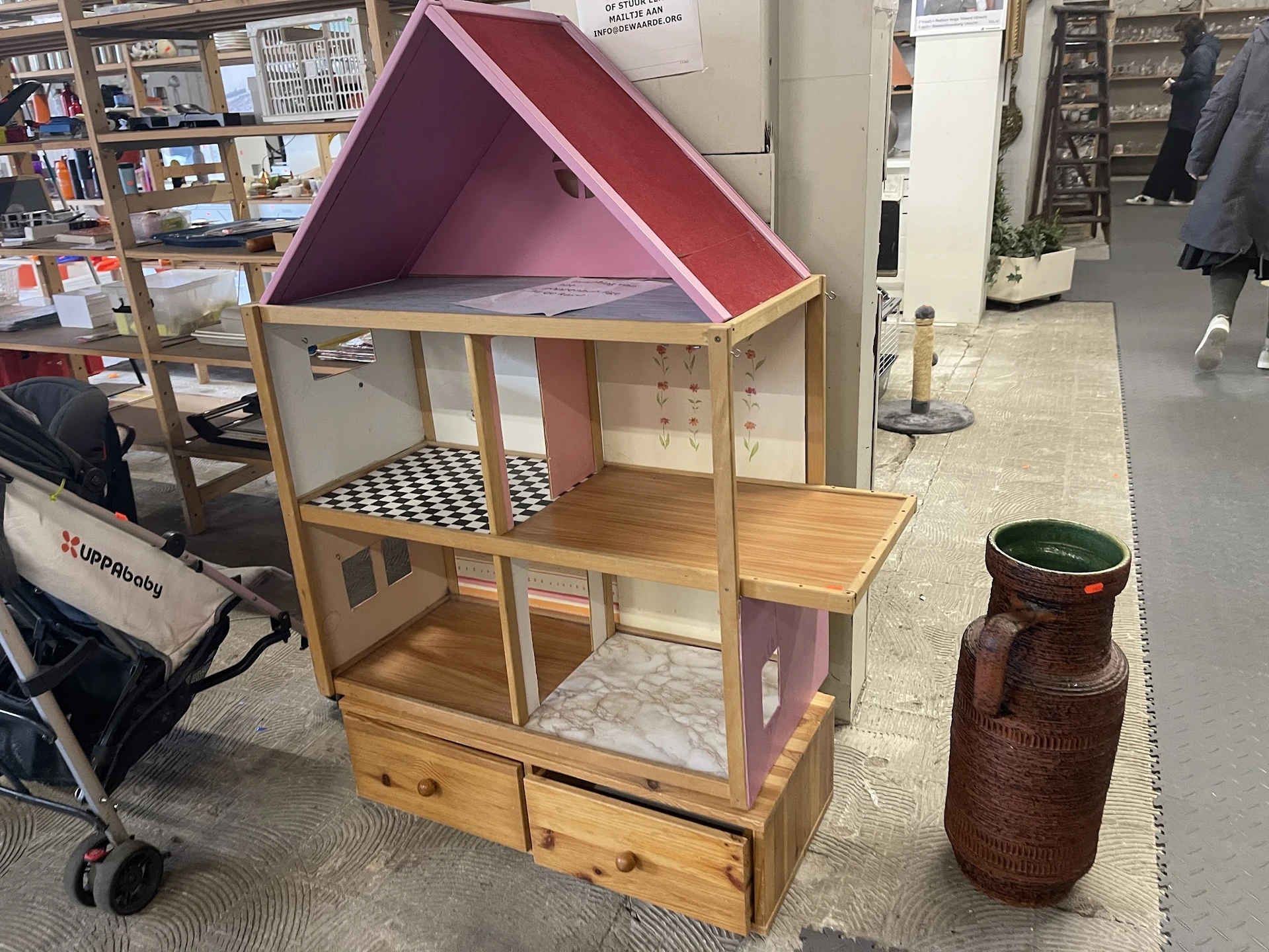 Houten poppenhuis met roze dak en inrichting, staand in een kringloopwinkel