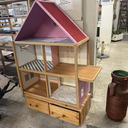 Houten poppenhuis met roze dak en inrichting, staand in een kringloopwinkel