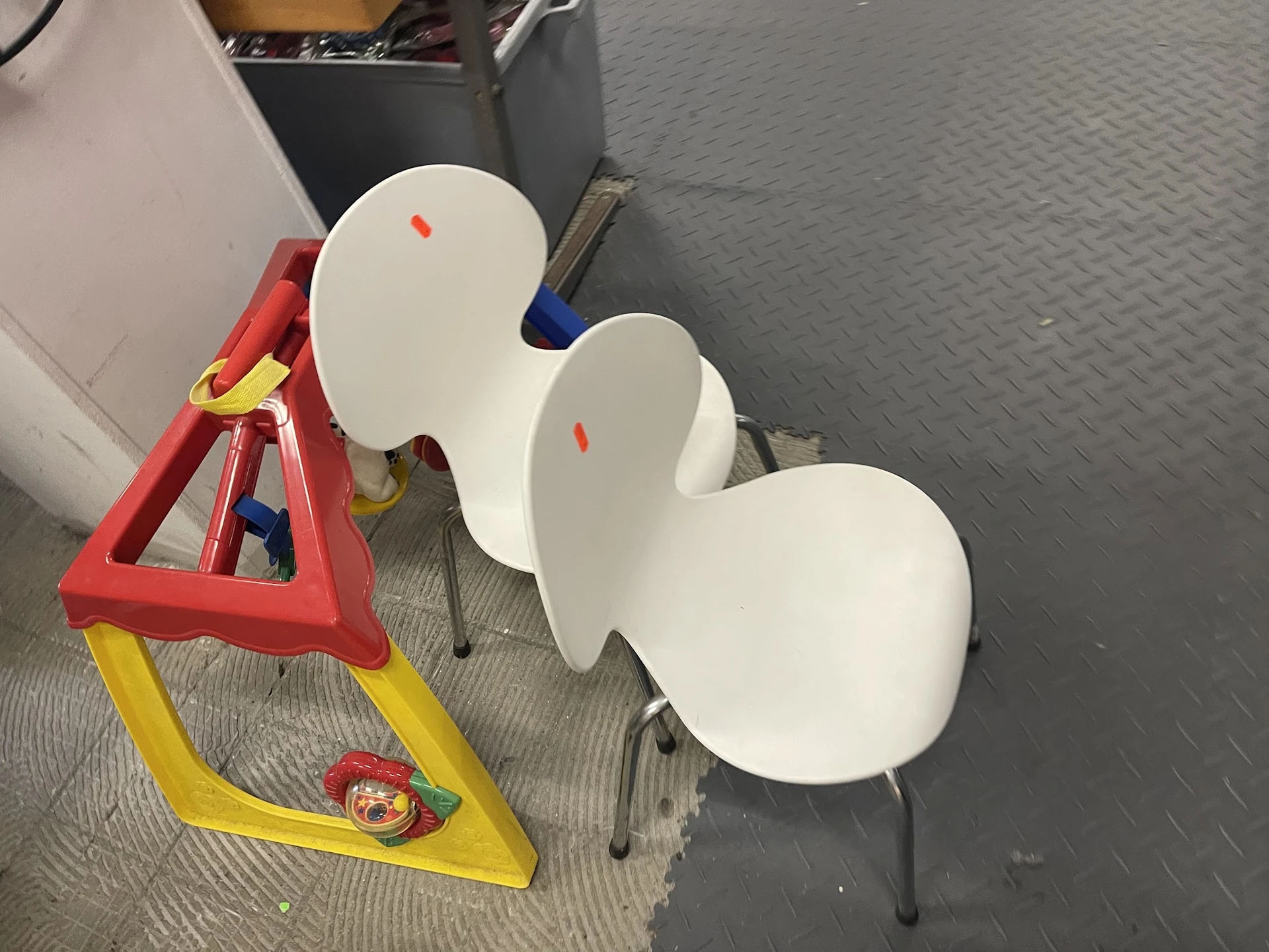 Drie witte kunststof stoelen en een rode/gele werkklem op grijze fabrieksgrond