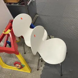 Drie witte kunststof stoelen en een rode/gele werkklem op grijze fabrieksgrond