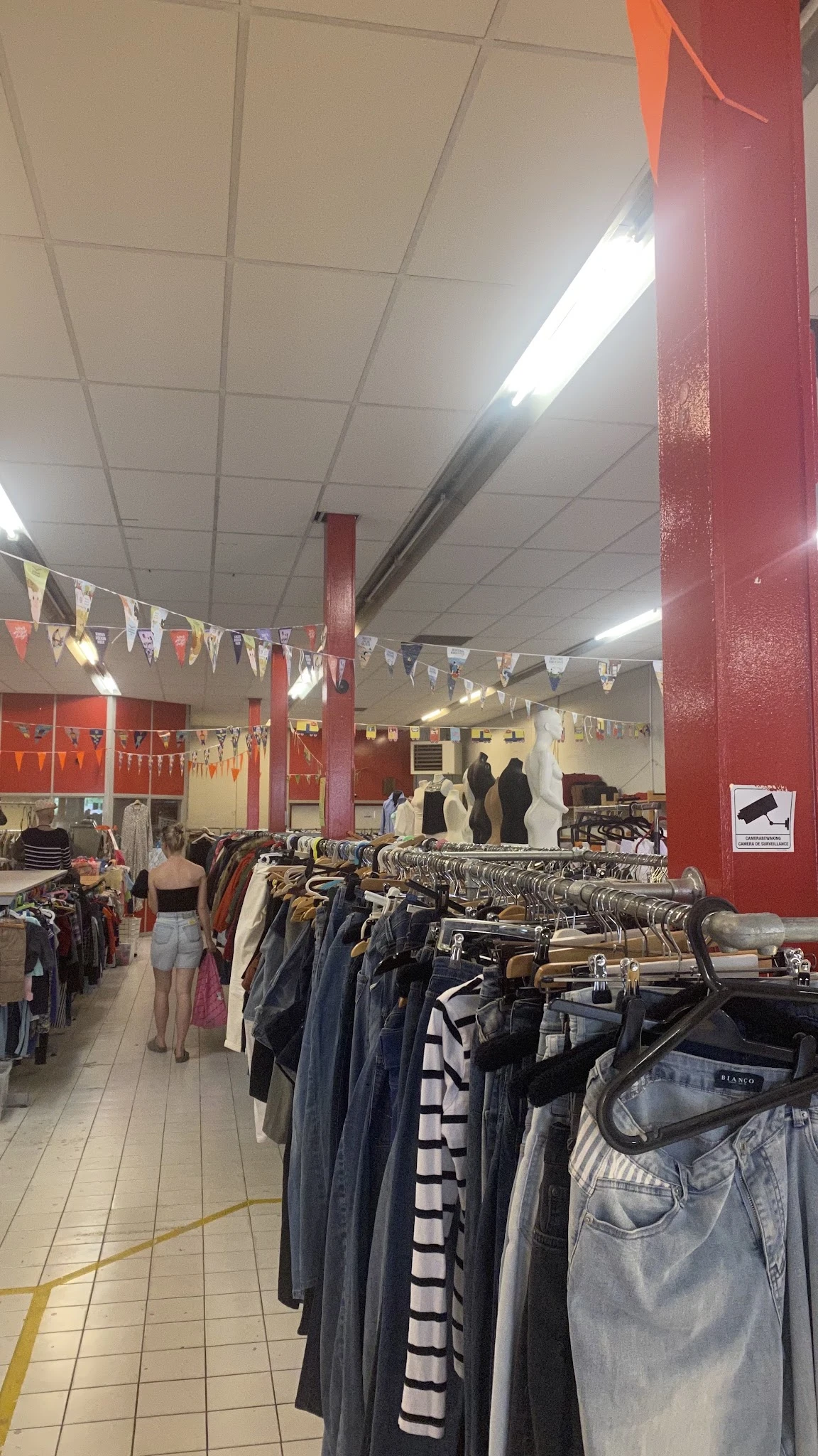 Winkelvloer met kledingrekken, rode zuilen en decoratie in een kringloopwinkel