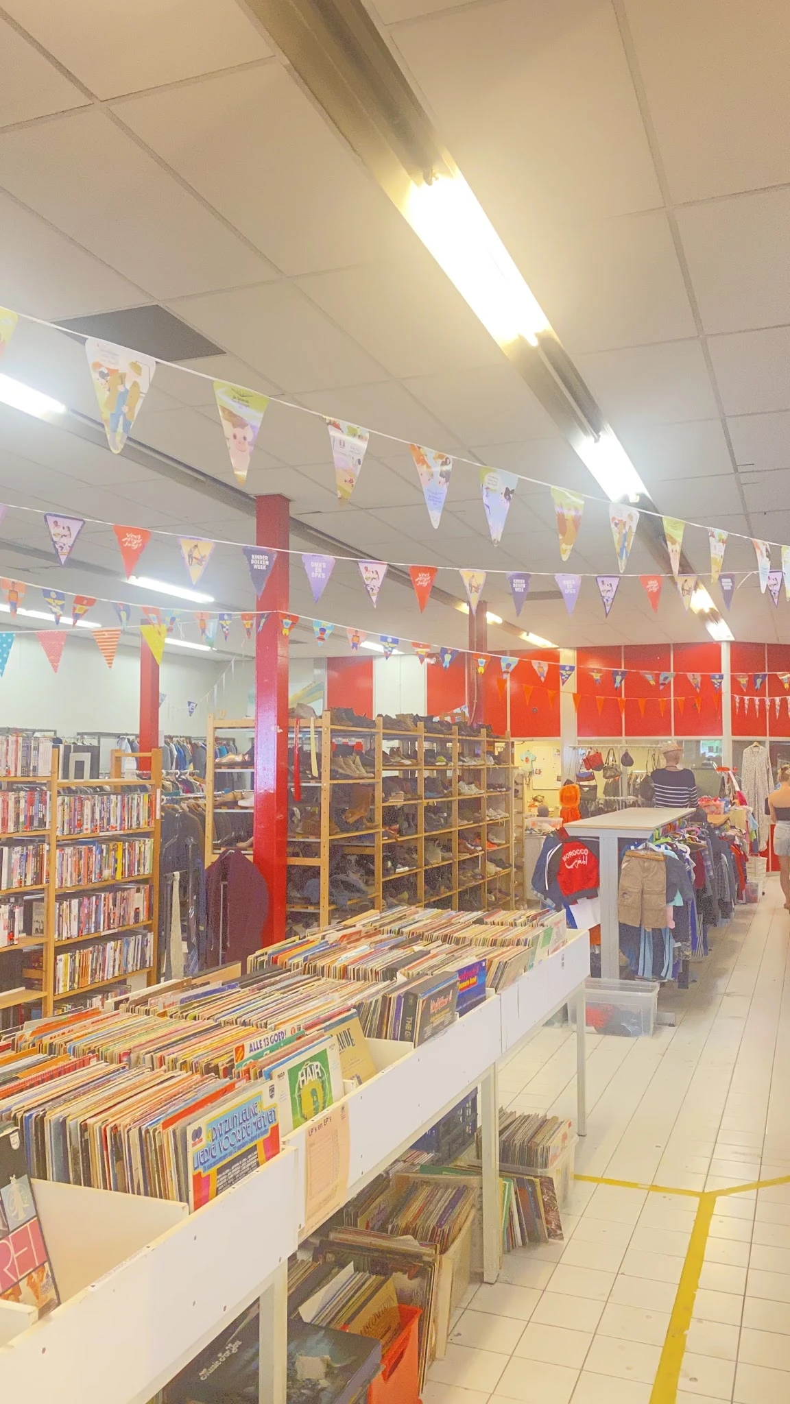 Winkelinterieur met boekenrekken aan de linkerkant, kleding op hangers aan de rechterkant, en kleurrijke vlaggenslinger als d