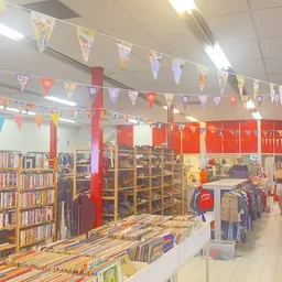 Winkelinterieur met boekenrekken aan de linkerkant, kleding op hangers aan de rechterkant, en kleurrijke vlaggenslinger als d