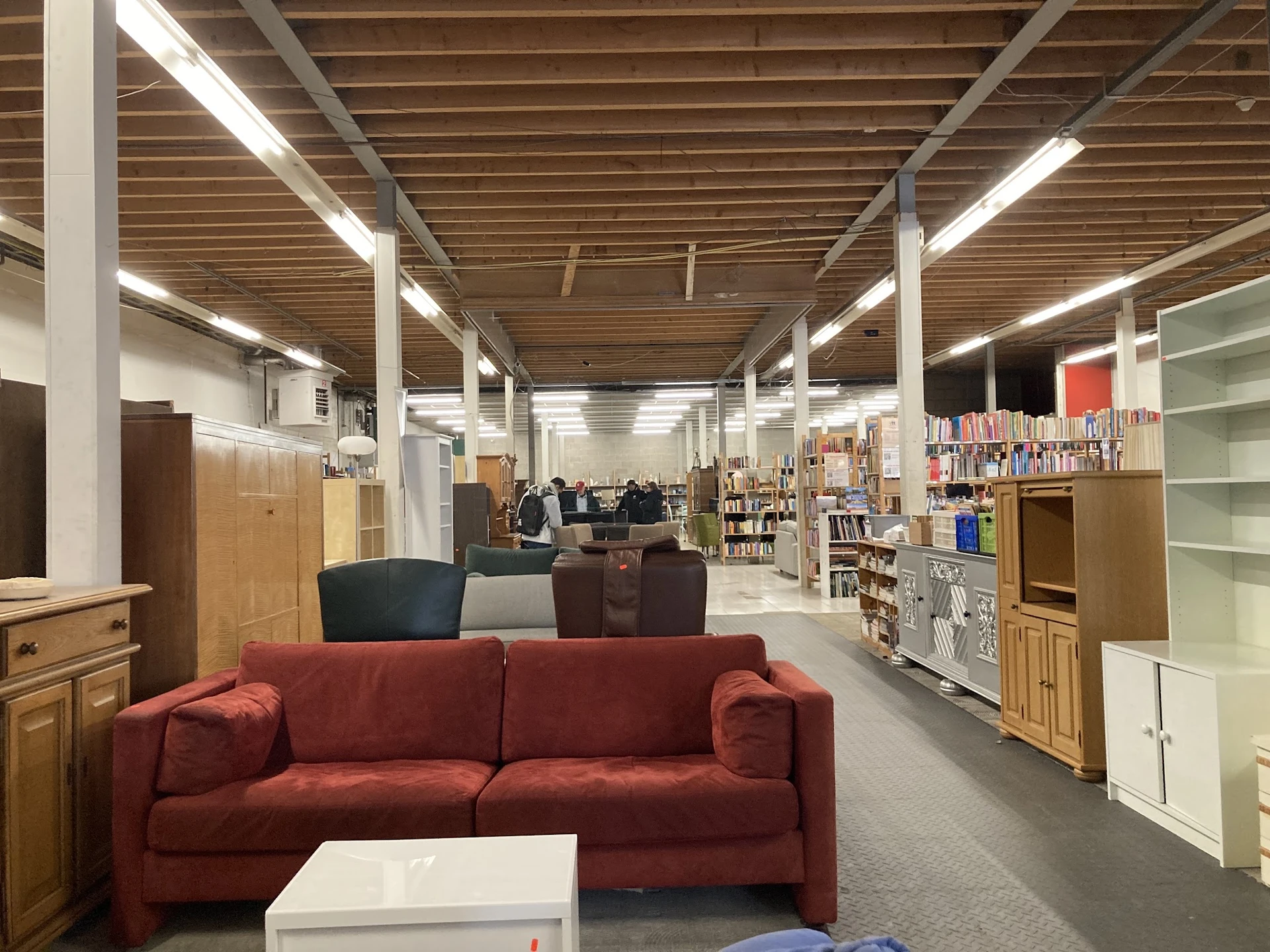 Winkelvloer met rode bank, houten meubels, boekenkasten en voorraad in een kringloopwinkel