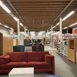 Winkelvloer met rode bank, houten meubels, boekenkasten en voorraad in een kringloopwinkel