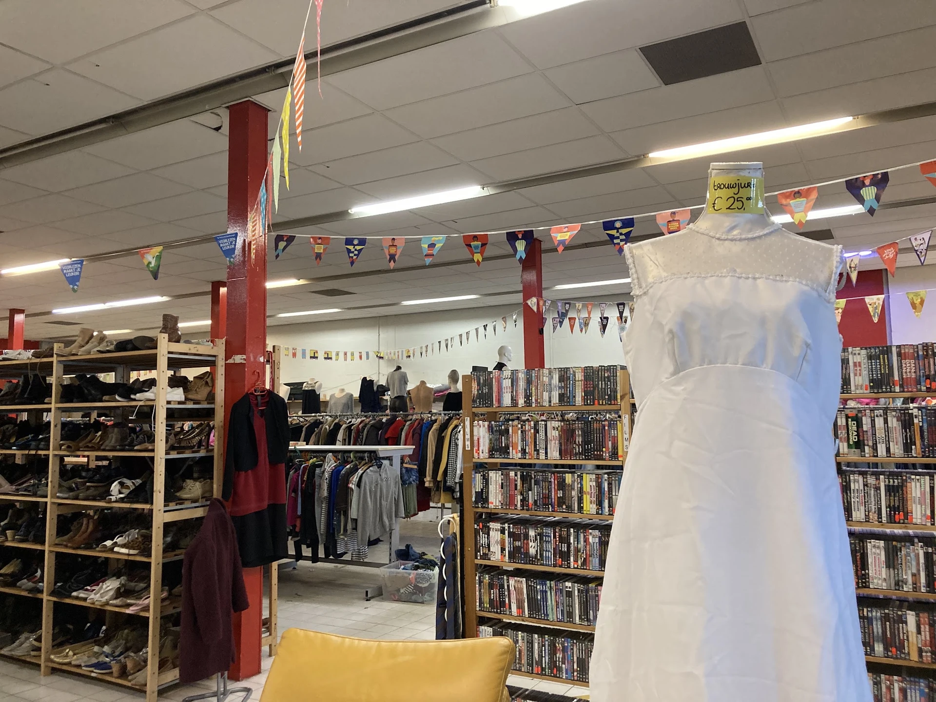 Binnenaanzicht van kringloopwinkel met dvd-rekken, kledingrekken, decoraties en een witte mannequin