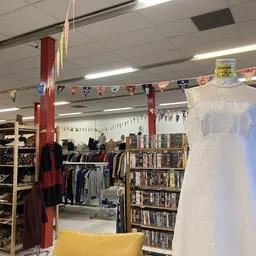 Binnenaanzicht van kringloopwinkel met dvd-rekken, kledingrekken, decoraties en een witte mannequin