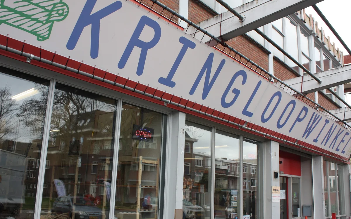 Gevel van kringloopwinkel met blauwe letters op rood winkelfront en grote glazen ramen