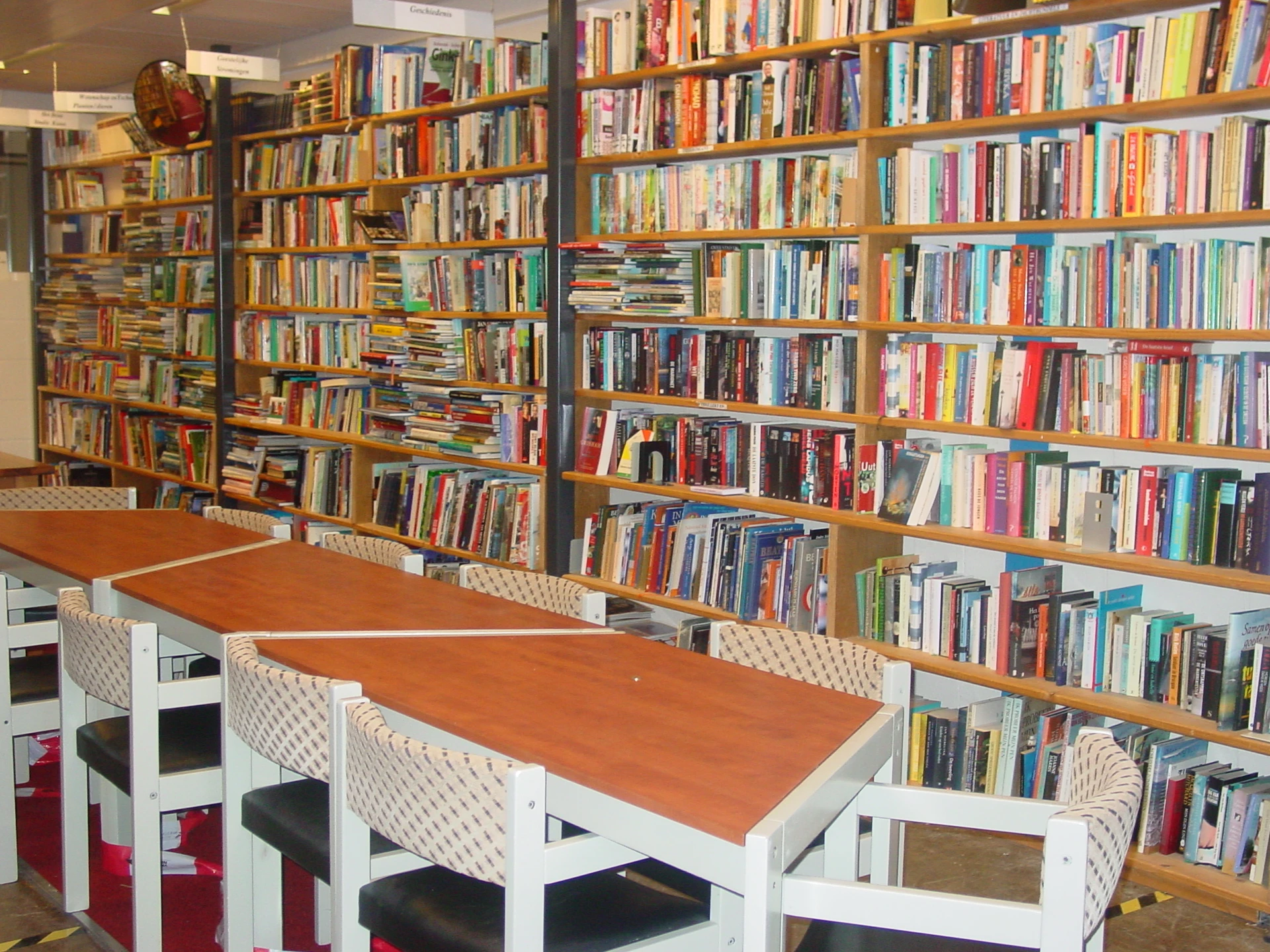 Boekenkasten vol met tweedehands boeken en een tafel met stoelen in de winkel