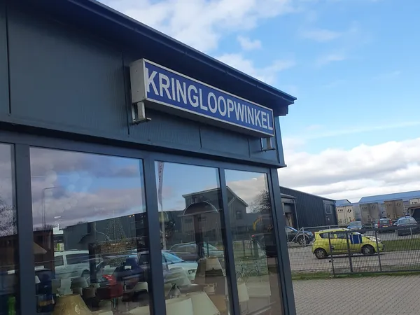 Gevel van kringloopwinkel De Wolden met donkerblauwe uithangteken en grote ramen, parkeerplaats zichtbaar