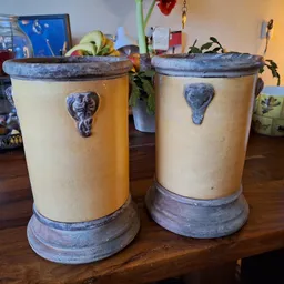 Twee decoratieve aardewerk vazen met blauwe accenten en deksels op een houten tafel