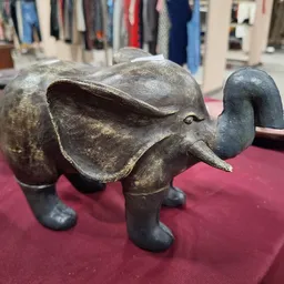 Grijsmetalen decoratief olifantje op rood tafelkleed in de winkel