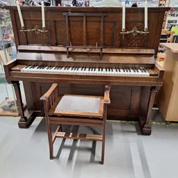 Donkerbruin houten piano met pianokruk in een kringloopwinkel