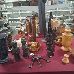 Uitgestalde decoratieve items op roze doek: houten beelden, stenen vazen, metalen figuren en houten schalen
