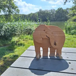 Houten olifantbeeldje op een houten boardwalk met uitzicht op groene weiden en bomen