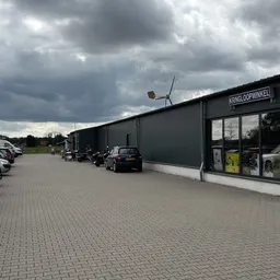 Zwarte gevel van kringloopwinkel met parkeerplaats en bewolkte hemel