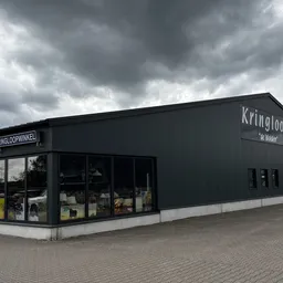 Zwart pand van kringloopwinkel met naam 'Kringloop' op gevel, grote ramen aan voorkant, bakstenen plein ervoor