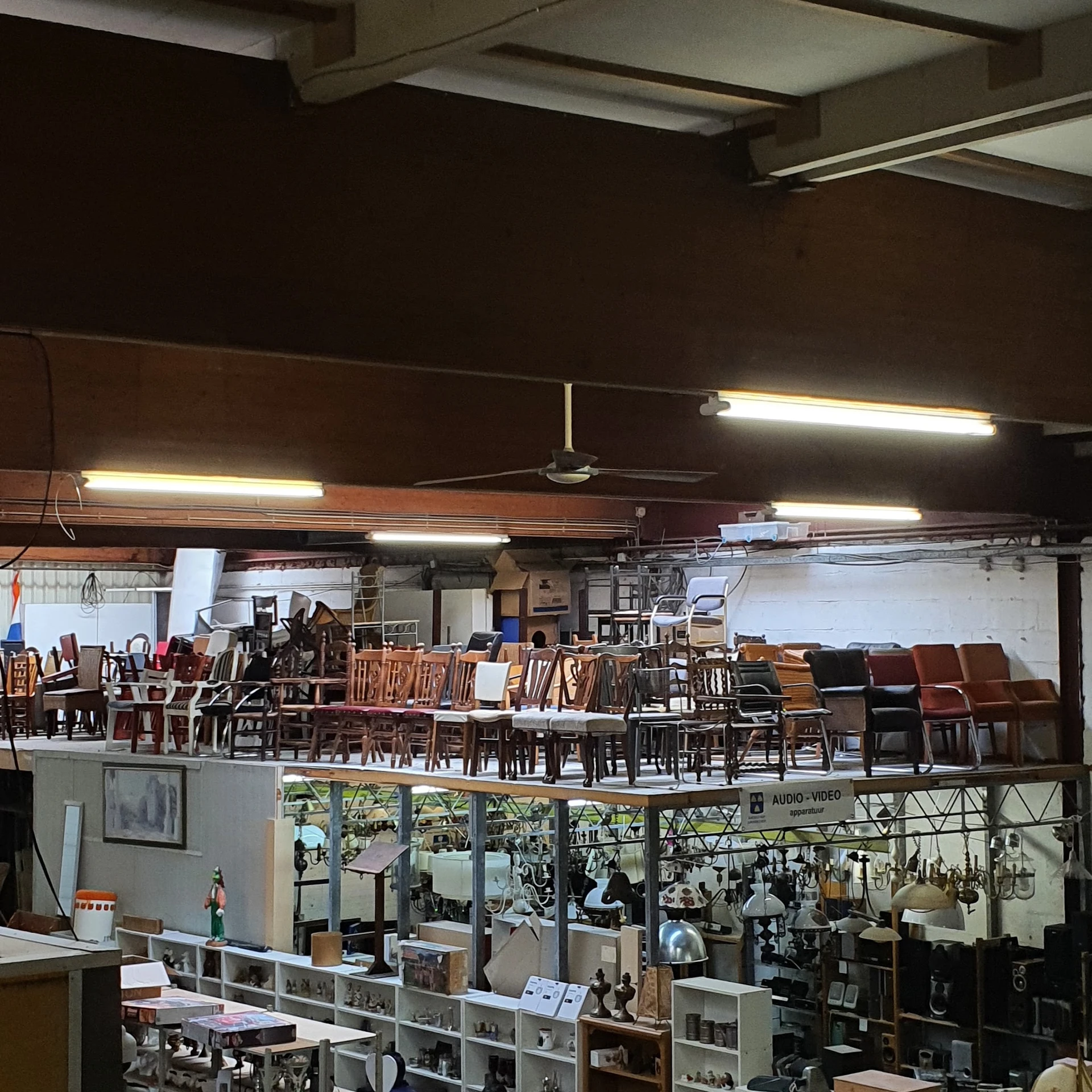 Bovenkant van winkelinterieur met fluorescente verlichting en veel houten stoelen en meubels uitgestald