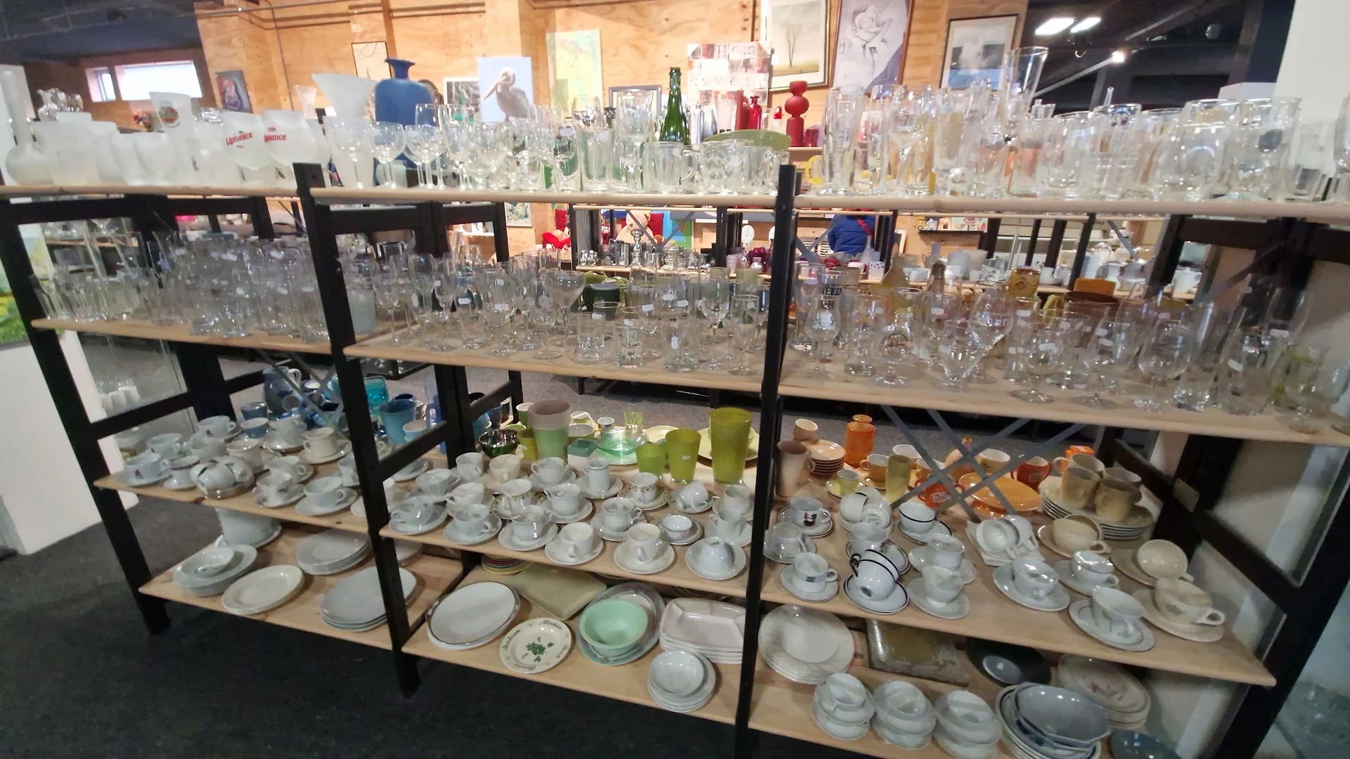 Zwarte stellingen volgesteld met glazen serviesgoed, glazen en aardewerk in een kringloopwinkel