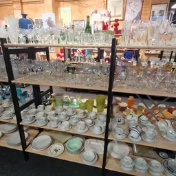Zwarte stellingen volgesteld met glazen serviesgoed, glazen en aardewerk in een kringloopwinkel