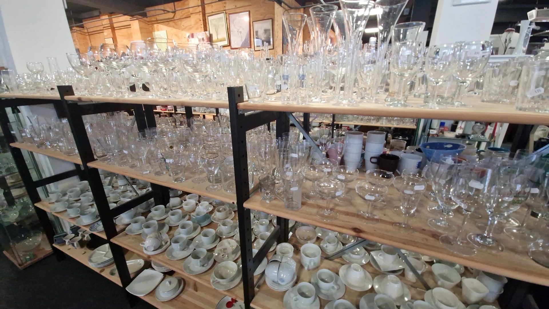 Houten stellingen met glazen serviesgoed, kristal en huishoudelijke artikelen in een kringloopwinkel