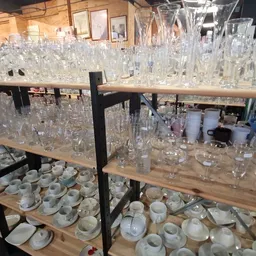 Houten stellingen met glazen serviesgoed, kristal en huishoudelijke artikelen in een kringloopwinkel