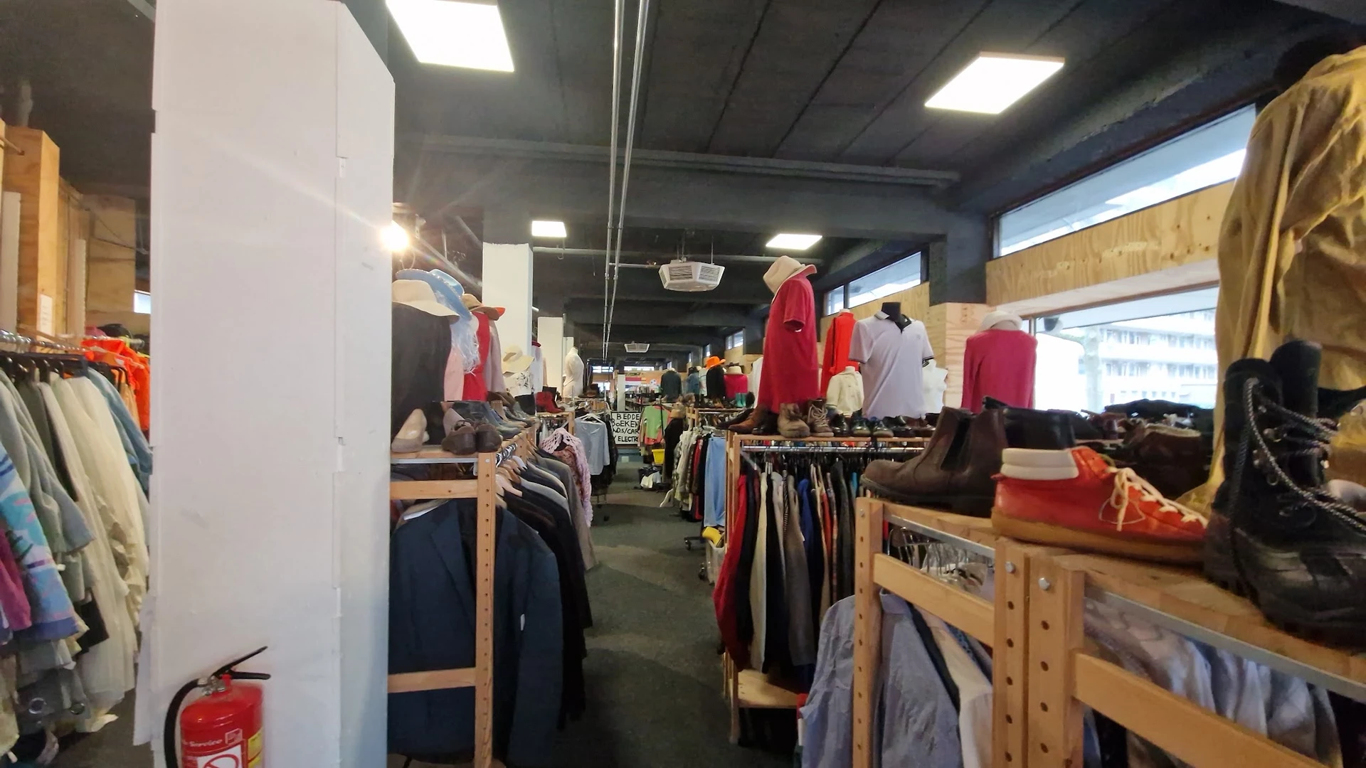 Winkelinterieur met kledingrekken, mannequins met rode en donkere kleding, houten stellingen en verlichte plafonds.