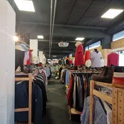 Winkelinterieur met kledingrekken, mannequins met rode en donkere kleding, houten stellingen en verlichte plafonds.