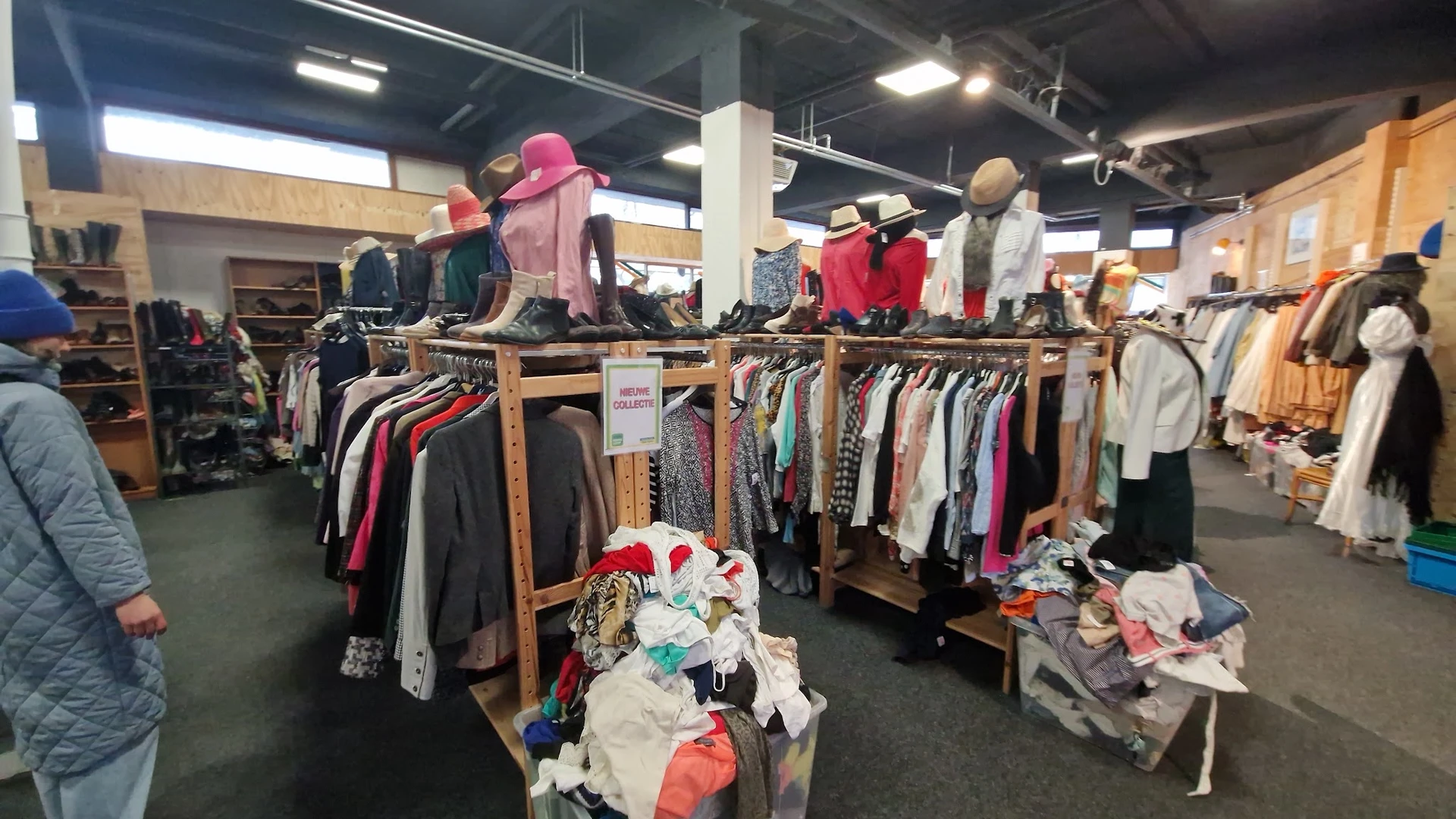 Houten rekken met tweedehands kleding en accessoires, mannequins met jassen en hoeden in een kringloopwinkel