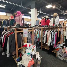Houten rekken met tweedehands kleding en accessoires, mannequins met jassen en hoeden in een kringloopwinkel