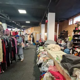 Winkelvloer met kledingrekken en tafels vol tweedehands kleding in een kringloopwinkel