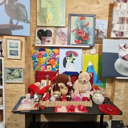 Uitgestalde tweedehandsartikelen op een tafel: knuffels, servies, kunstwerken en decoratieve items tegen een houten achtergro