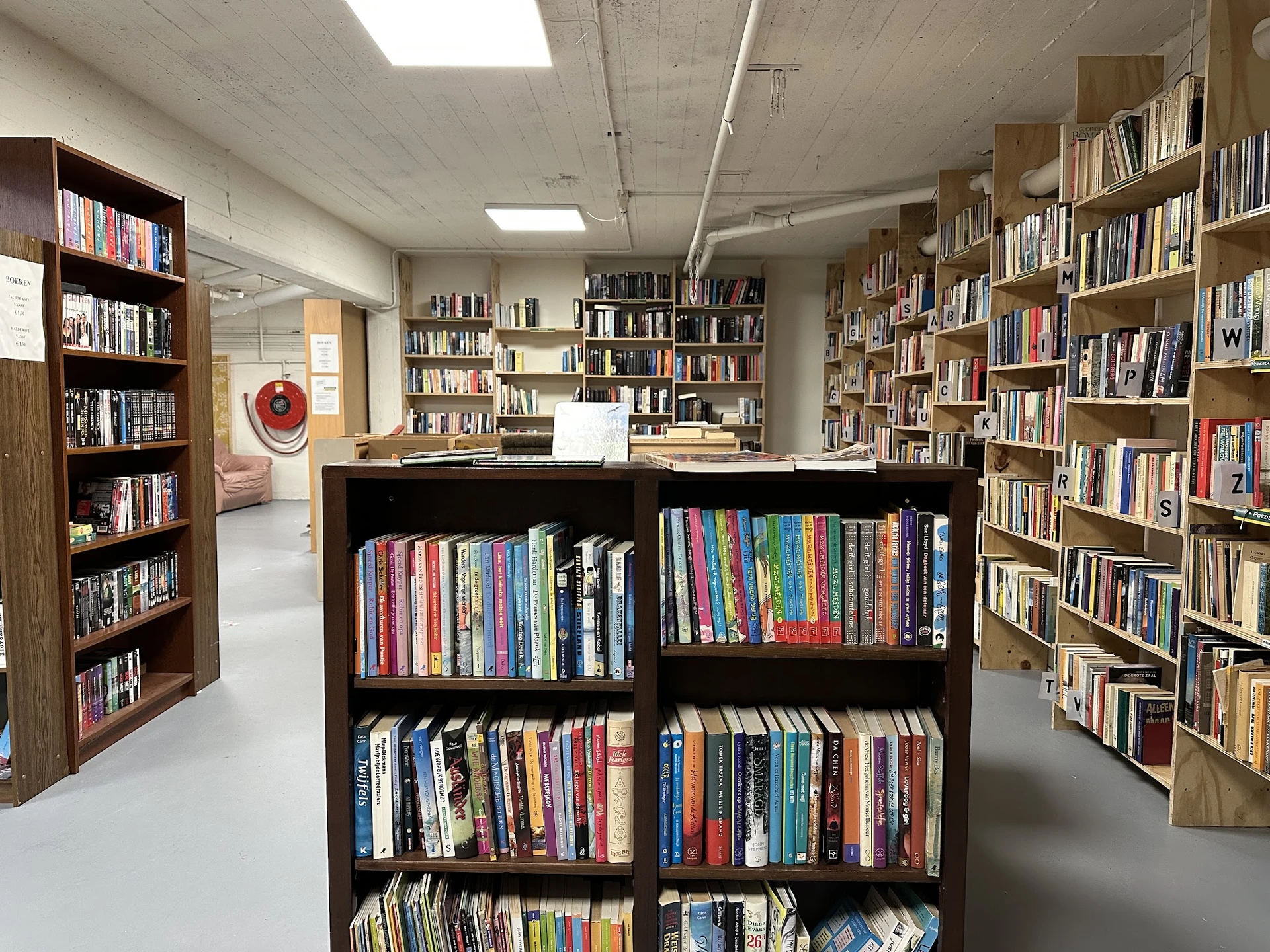 Binnenzicht van kringloopwinkel met boekenkasten en dvd-rekken langs de wanden en in het midden